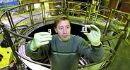 Marcus Knudson holds two flyer plates in his right hand and chambers of his high-tech gun in his left. In the background is the innermost sanctum of Sandia's Z accelerator, where a rapidly expanding magnetic field drives pellets faster than any mechanism on earth